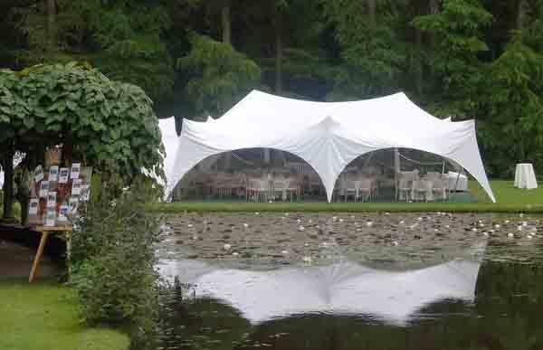 Elegant wedding marquee set up on the grassy shores of a serene country lake, beautifully decorated for a luxury wedding celebration with panoramic views of nature.