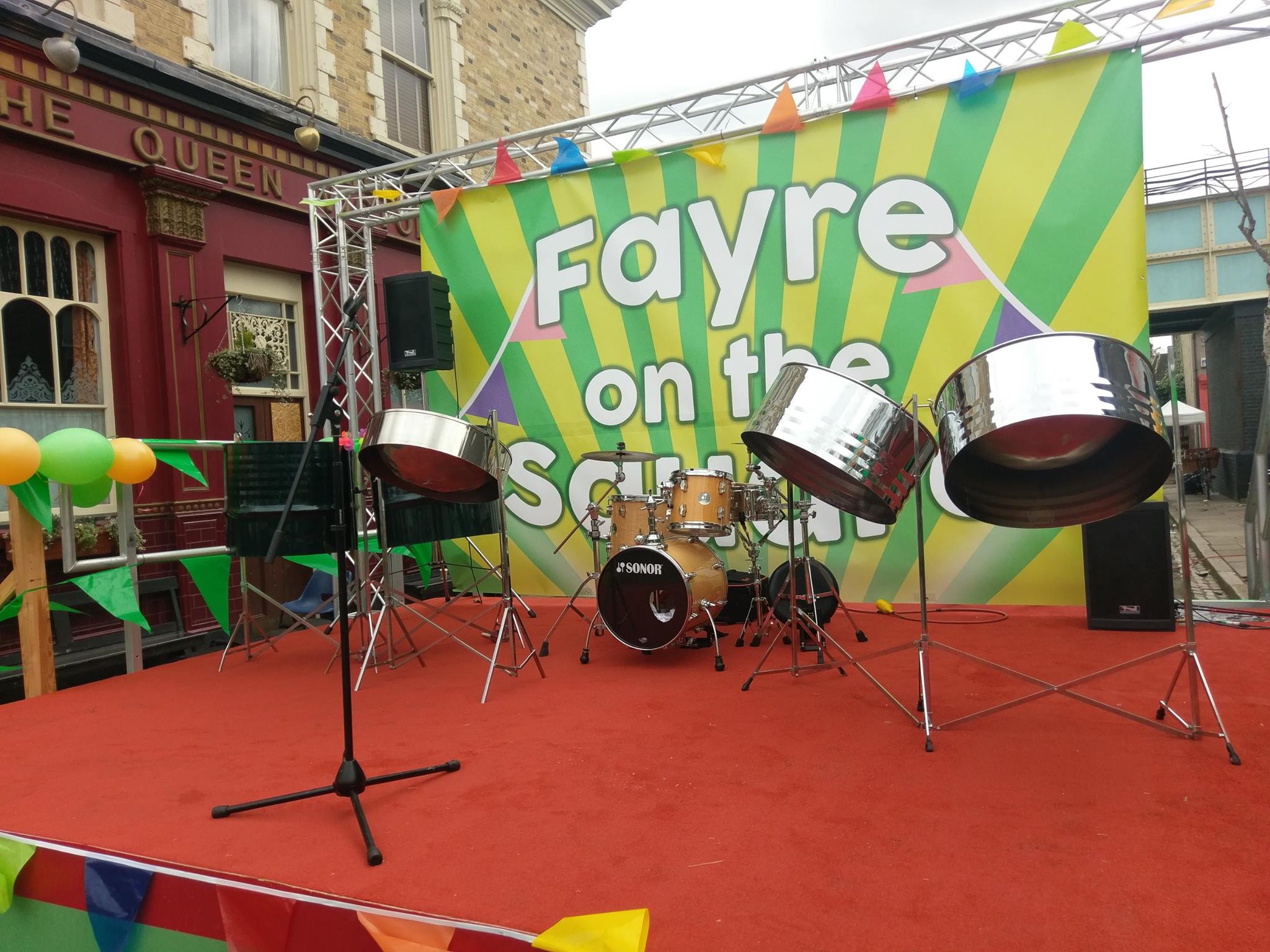 Five-piece Caribbean steel drum band performing at a vibrant party on the set of the TV show EastEnders, bringing lively music and festive atmosphere.