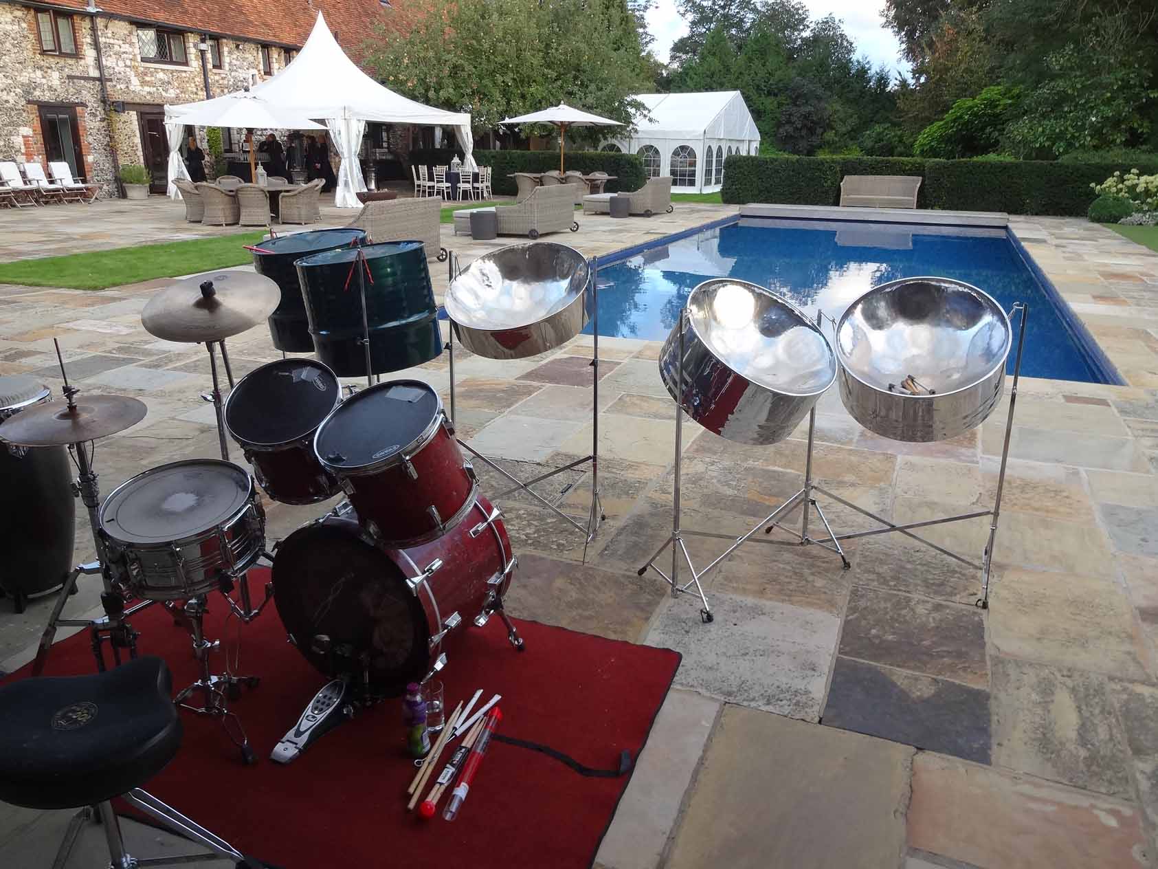 Five-piece Caribbean steel drum band set up beside a swimming pool at an exquisite summer party, providing lively entertainment and a festive atmosphere.