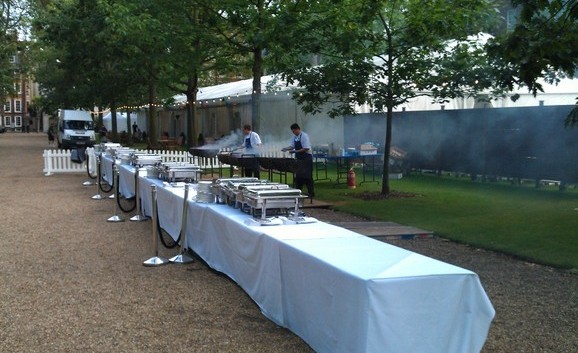 Catering team preparing tables for a corporate summer event at Gray's Inn, London, arranging elegant table settings and decor.