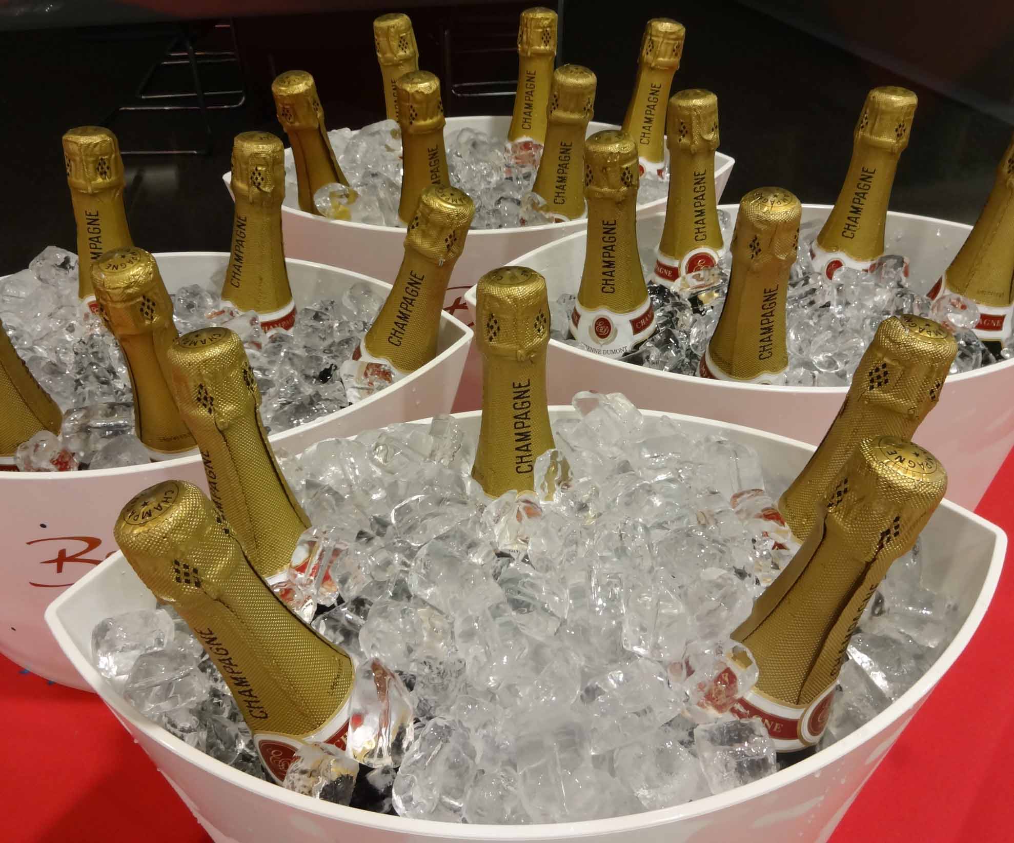 Four buckets filled with champagne bottles chilling on ice at a festive party, ready to be served to guests.