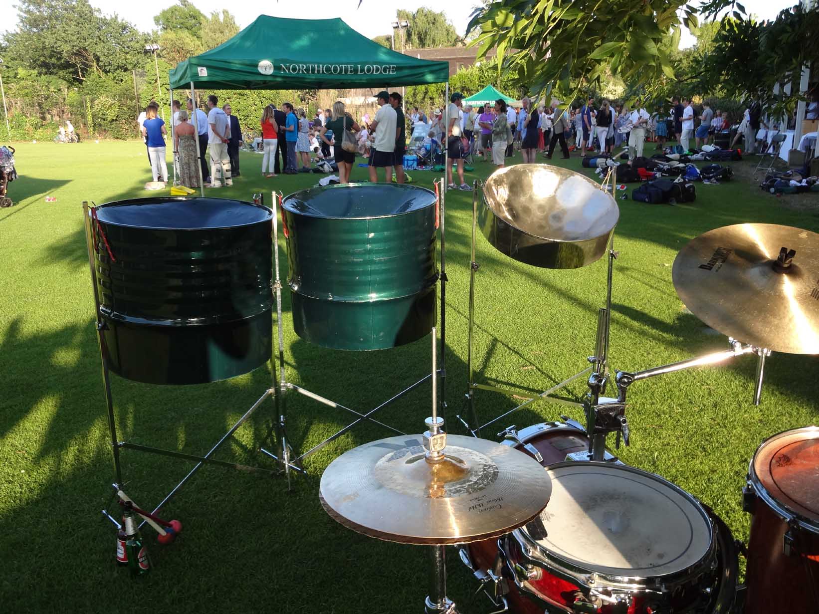Three-piece steel drum band performing at a corporate summer drinks party in the park, providing vibrant entertainment for the event.