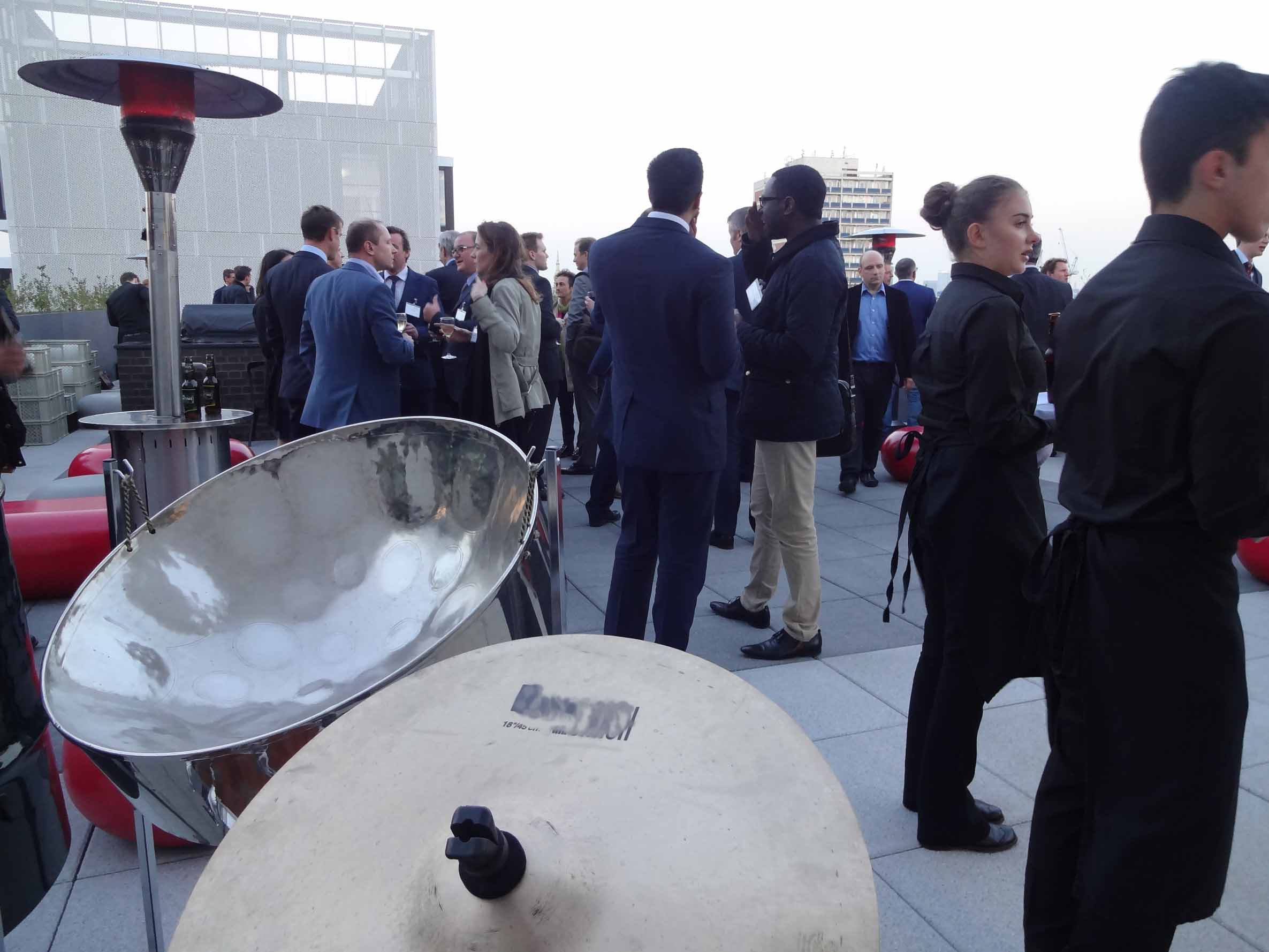 Three-piece steel drum band performing at a corporate summer drinks party on a roof terrace, providing vibrant entertainment for the event.