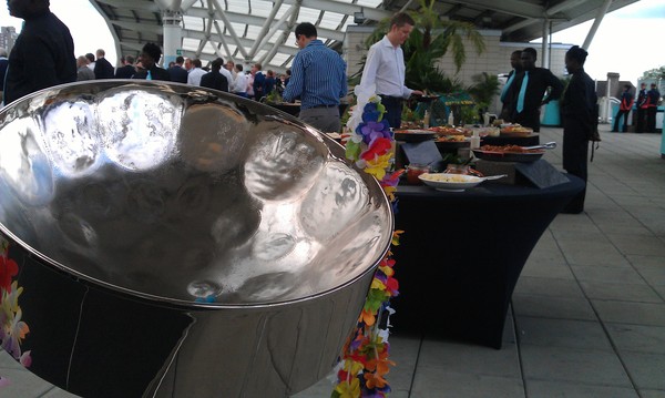 Close-up of a steel drum with corporate guests queuing for food in the background at a Kia Oval cricket event.