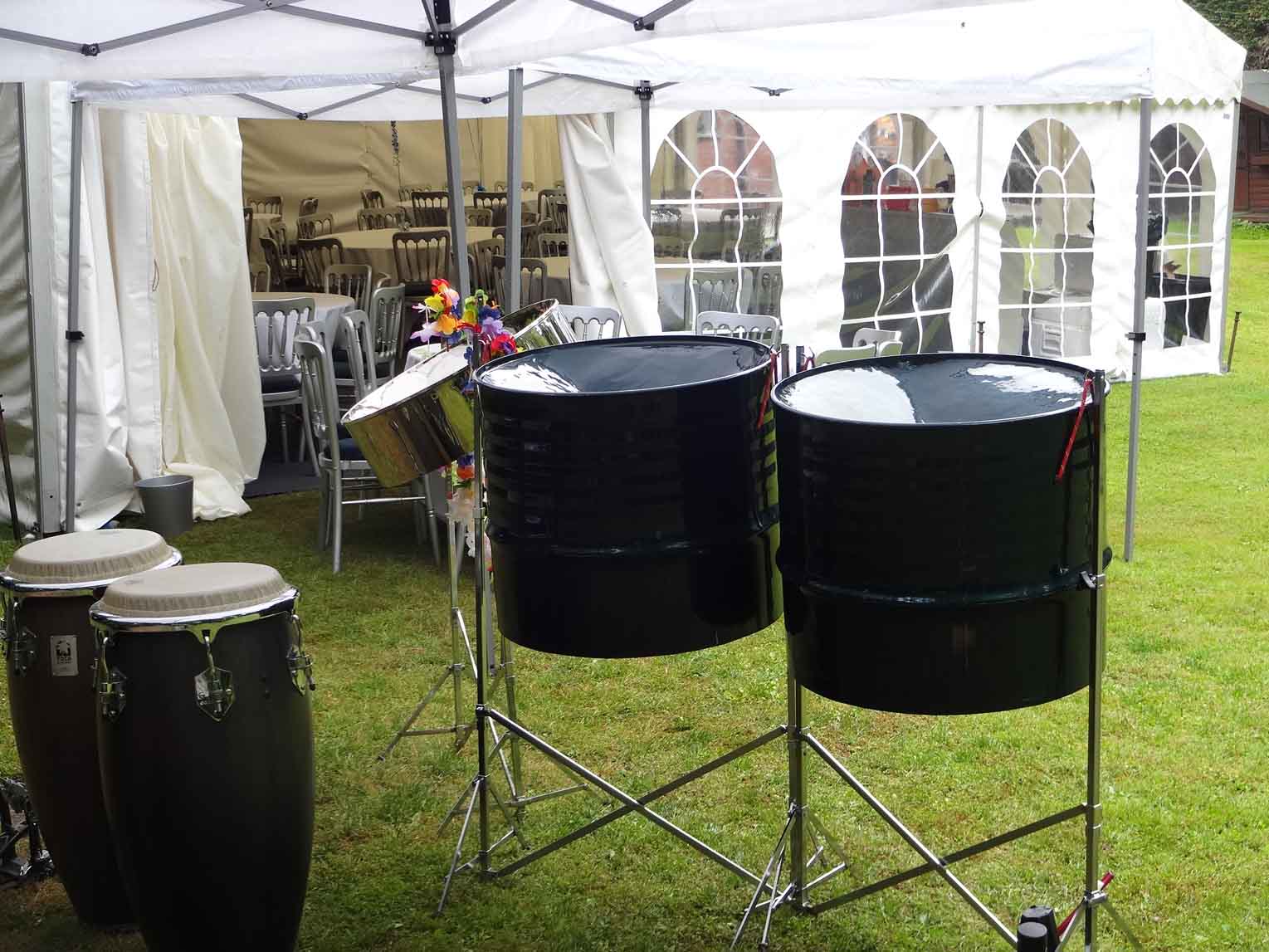 Three-piece steel drum band performing at a private summer drinks party outside a marquee, providing vibrant entertainment for the event.
